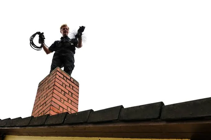 Chimney sweep standing above a brick chimney with cleaning tools
