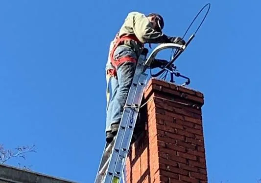 Technician inspecting a brick chimney from a secured ladder
